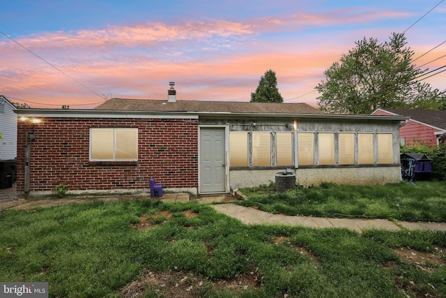 back of property at dusk with brick siding, a chimney, and central AC