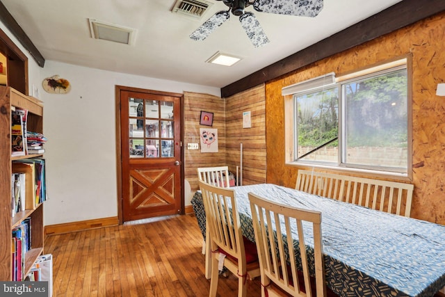 dining area with wood-type flooring, ceiling fan, baseboards, and wood walls