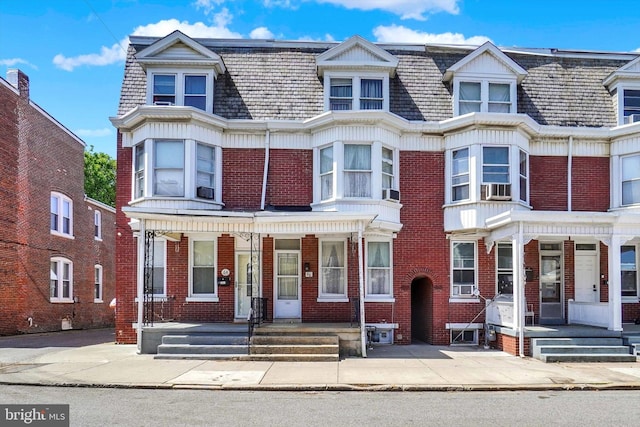 multi unit property featuring brick siding, mansard roof, covered porch, and cooling unit