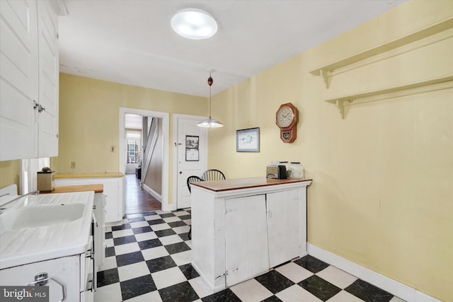 kitchen with a sink, dark floors, a peninsula, decorative light fixtures, and white cabinetry
