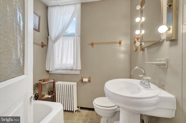 bathroom with baseboards, radiator heating unit, toilet, and a tub to relax in