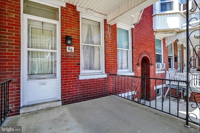 entrance to property featuring covered porch, cooling unit, and brick siding
