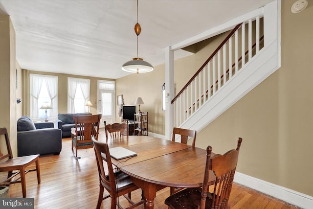 dining area with baseboards, light wood-style flooring, and stairway
