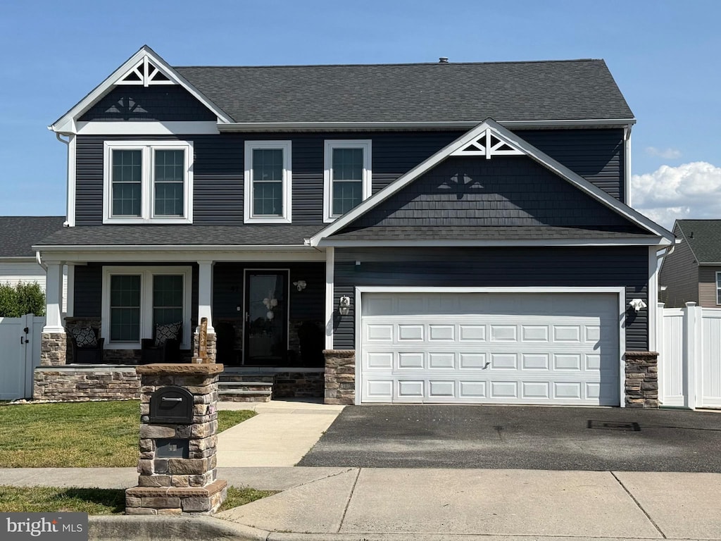craftsman inspired home featuring covered porch, fence, driveway, and stone siding