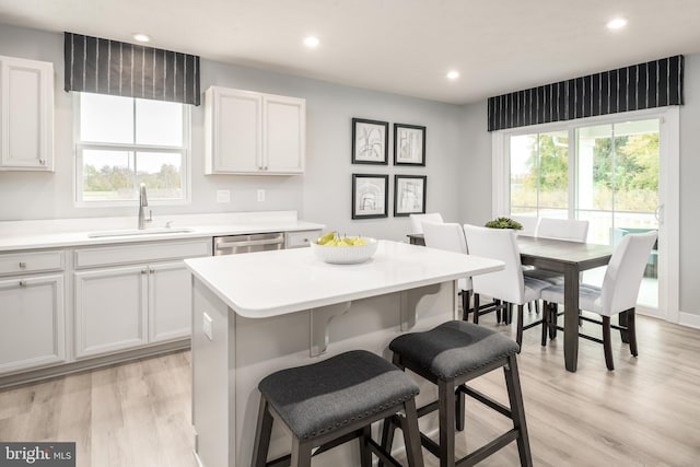 kitchen featuring a healthy amount of sunlight, a breakfast bar area, a center island, a sink, and light wood-style flooring