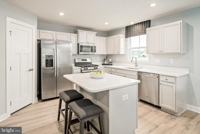 kitchen featuring a kitchen bar, appliances with stainless steel finishes, a sink, white cabinets, and light wood-style floors
