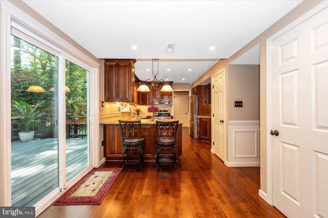 kitchen with wainscoting, stainless steel appliances, a peninsula, and dark wood-style floors