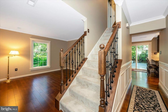 stairs with wood-type flooring, baseboards, crown molding, and a wainscoted wall