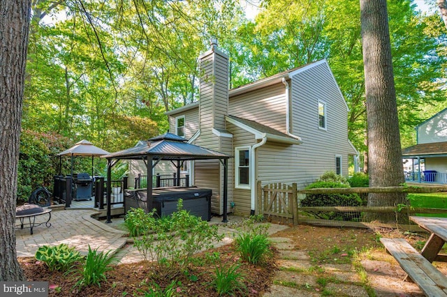 back of house featuring fence, a gazebo, a hot tub, a chimney, and a patio area