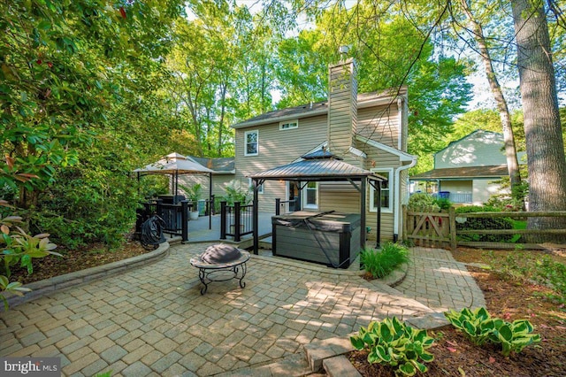 rear view of house with a chimney, a patio area, a hot tub, a gazebo, and fence