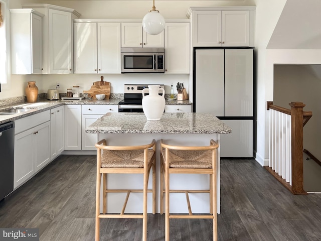 kitchen with dark wood-style flooring, appliances with stainless steel finishes, white cabinets, and light stone countertops