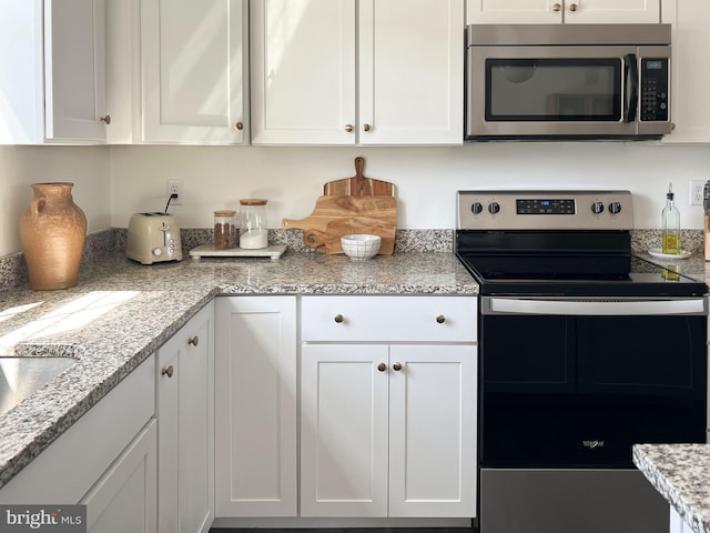 kitchen with light stone counters, white cabinetry, and stainless steel appliances