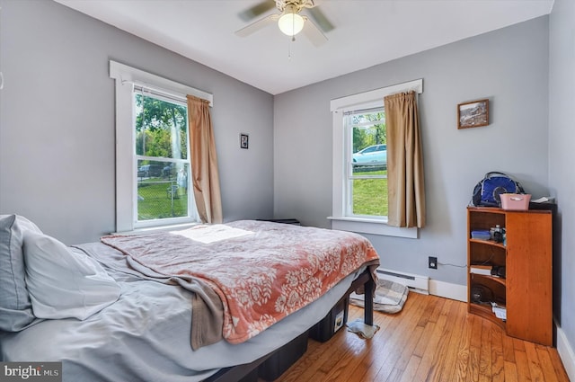 bedroom with wood-type flooring, a baseboard radiator, baseboards, and multiple windows