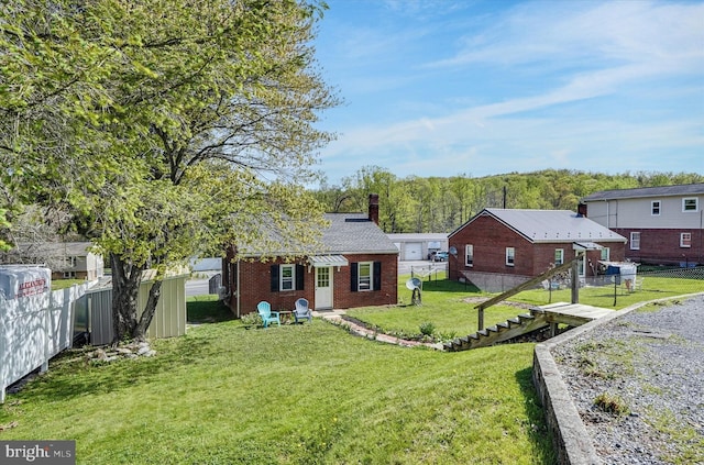 rear view of house featuring fence, a chimney, brick siding, stairs, and a lawn