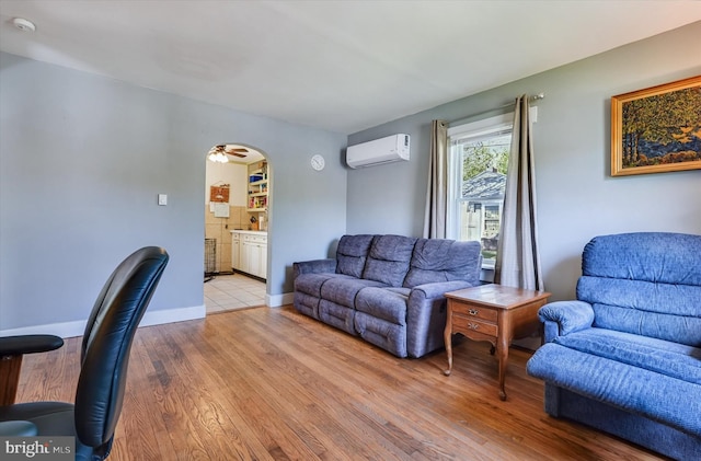 living room featuring baseboards, a wall mounted air conditioner, arched walkways, a ceiling fan, and light wood finished floors