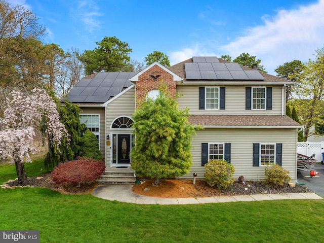 view of front facade with roof with shingles, roof mounted solar panels, and a front yard