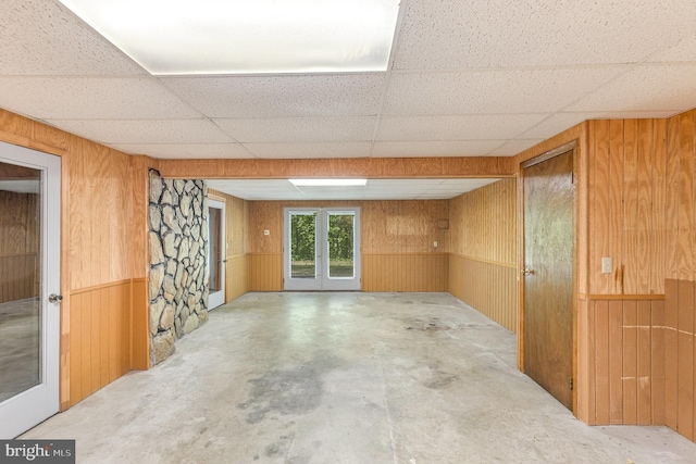 empty room featuring wood walls, concrete floors, and a drop ceiling
