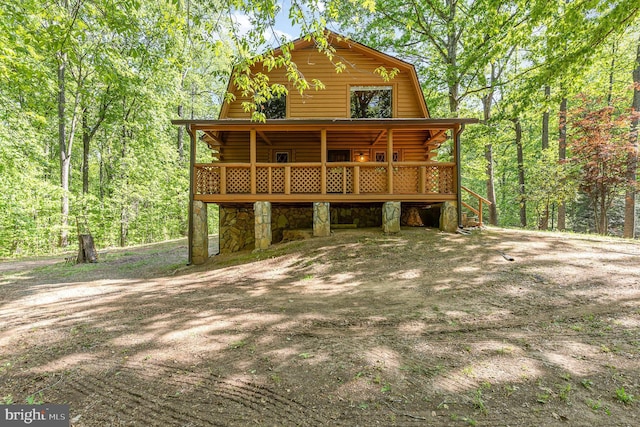 view of front facade with a deck, log exterior, a gambrel roof, and a forest view