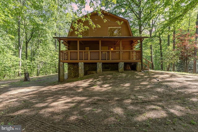 view of front of property with a wooded view, a wooden deck, log exterior, and a gambrel roof