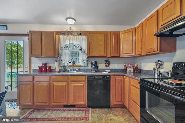 kitchen with brown cabinetry, dark countertops, under cabinet range hood, a sink, and black appliances