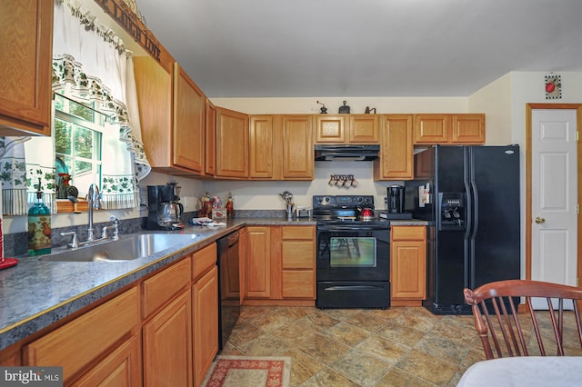 kitchen featuring stone finish flooring, dark countertops, a sink, black appliances, and under cabinet range hood