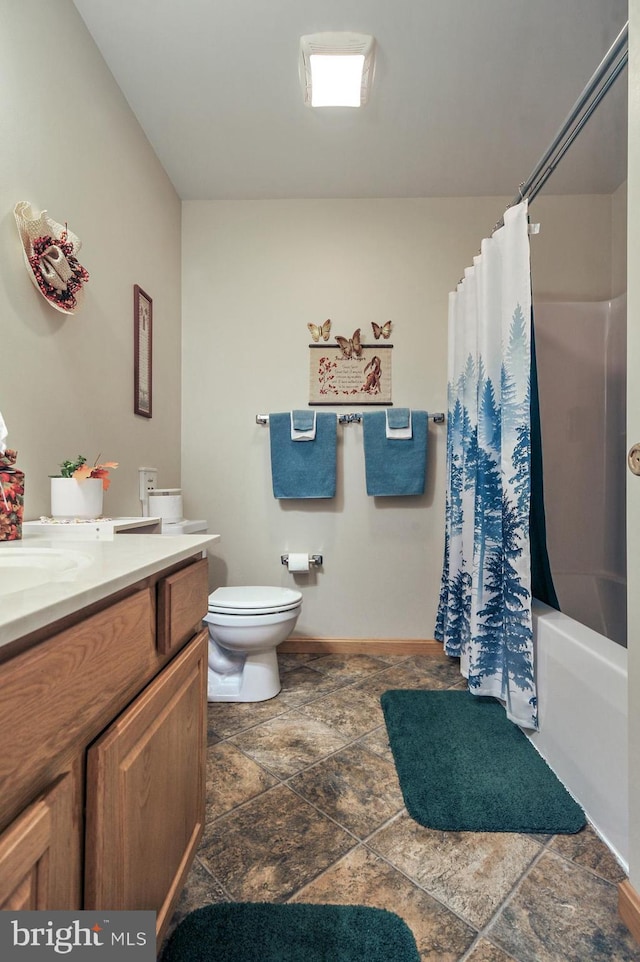 full bath with stone finish flooring, vanity, baseboards, toilet, and shower / tub combo with curtain