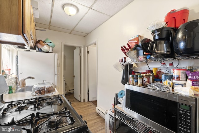 kitchen with a paneled ceiling, light wood-type flooring, freestanding refrigerator, stainless steel microwave, and range with gas stovetop
