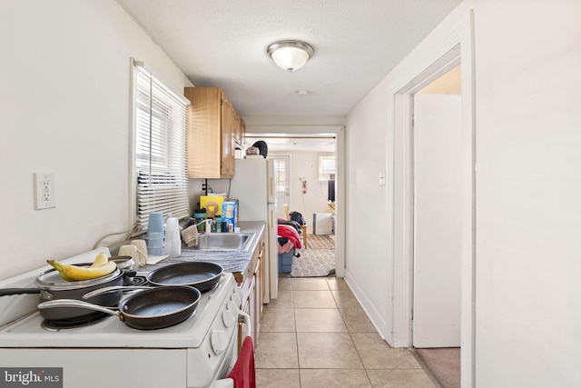 kitchen with electric range, a textured ceiling, a sink, light countertops, and light tile patterned floors