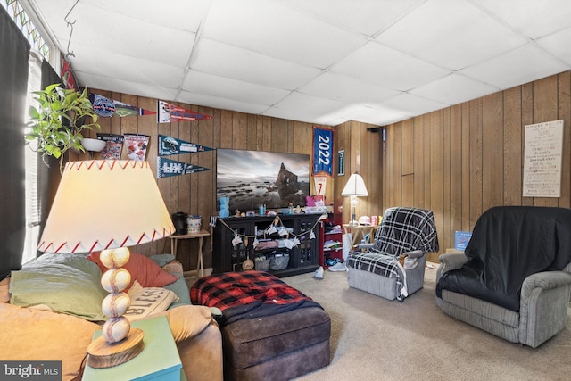 carpeted living area featuring wood walls and a paneled ceiling