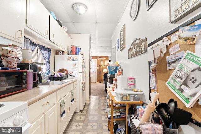 kitchen with freestanding refrigerator, black microwave, a drop ceiling, light countertops, and range