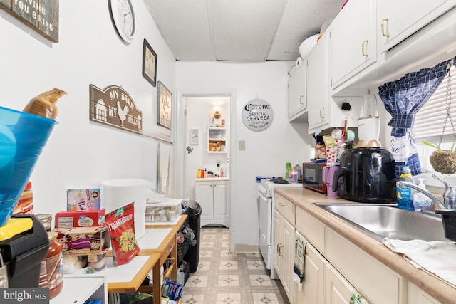 kitchen with white gas range, a sink, light countertops, white cabinets, and light floors