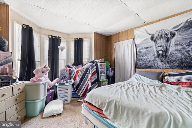 carpeted bedroom featuring wood walls and a drop ceiling
