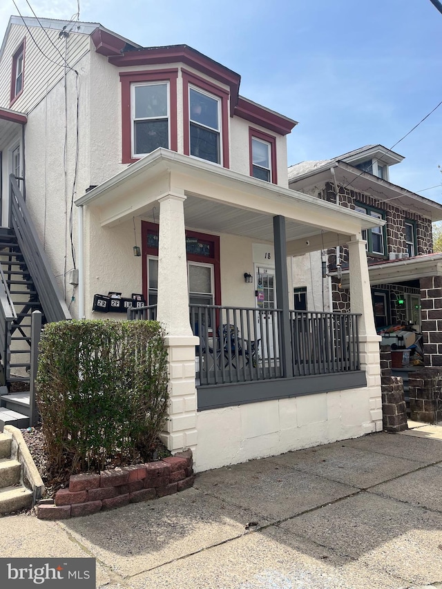view of front facade featuring stucco siding, a porch, and stairway