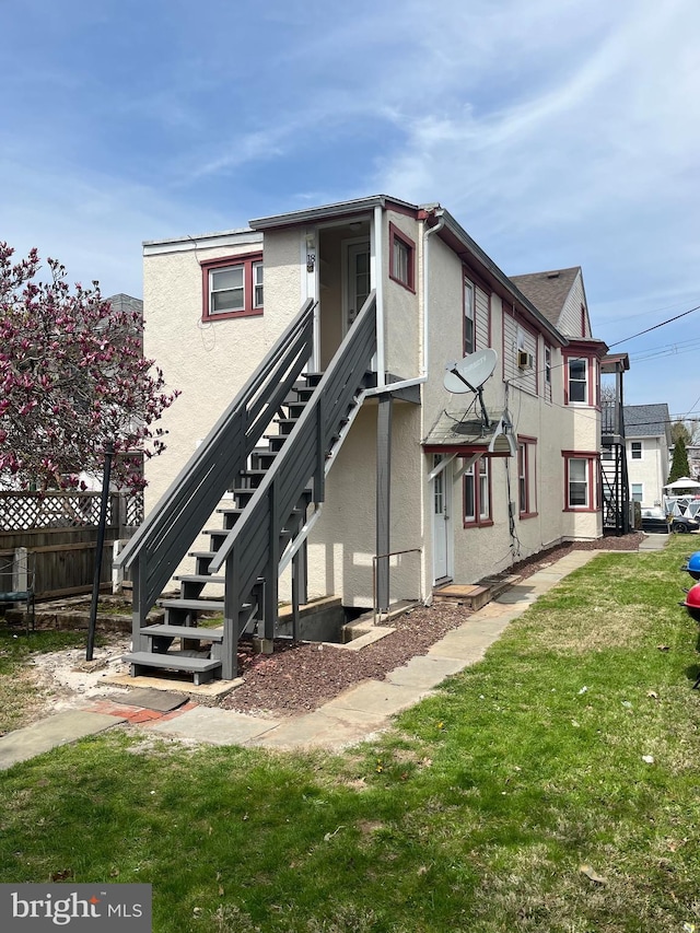 exterior space with stairs, stucco siding, a yard, and fence