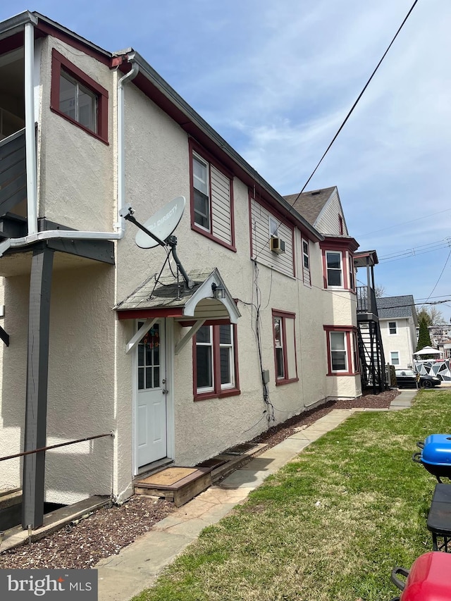 rear view of house with a lawn, stucco siding, and cooling unit