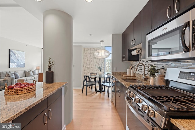 kitchen featuring light stone countertops, tasteful backsplash, a sink, light wood finished floors, and appliances with stainless steel finishes