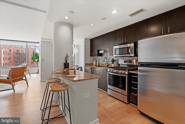 kitchen featuring appliances with stainless steel finishes, a kitchen bar, light wood-style flooring, and visible vents