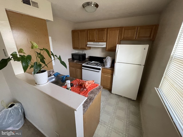 kitchen featuring visible vents, a peninsula, white appliances, light floors, and under cabinet range hood
