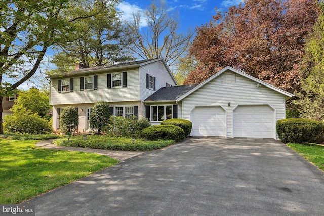 colonial house featuring an attached garage, a chimney, driveway, and a front yard