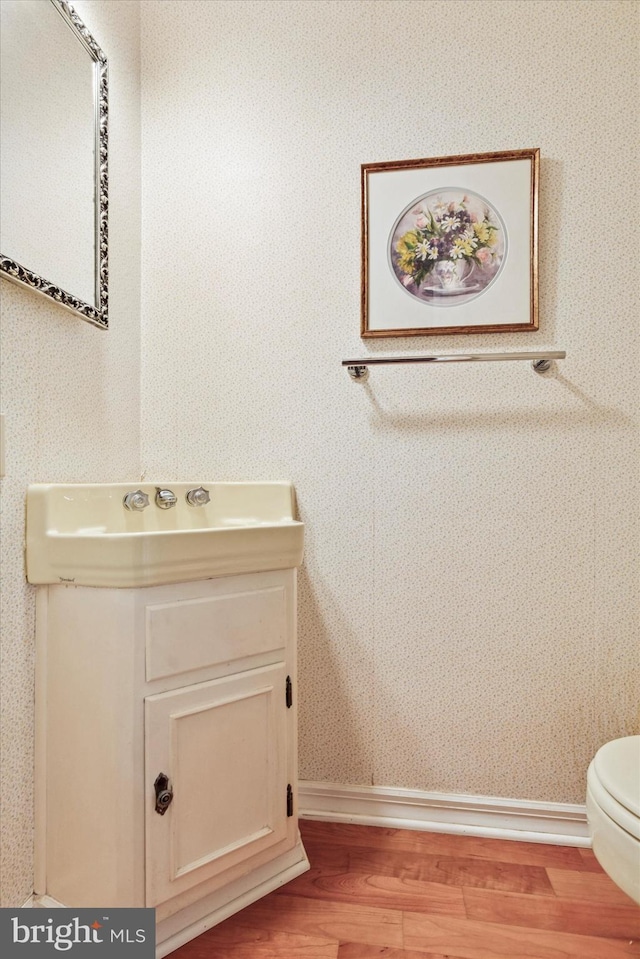 bathroom with vanity, wood finished floors, toilet, baseboards, and wallpapered walls