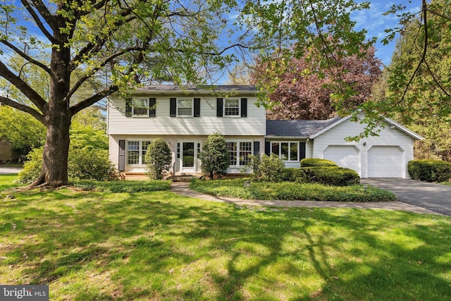 colonial home with an attached garage, a front lawn, and driveway