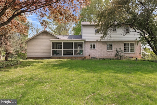 rear view of property featuring a sunroom, a lawn, and brick siding