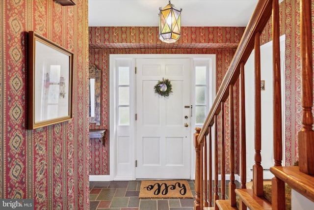 entrance foyer featuring stairway, wallpapered walls, and stone finish flooring