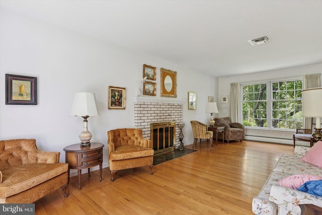 living room with a brick fireplace, visible vents, baseboard heating, and light wood-style flooring