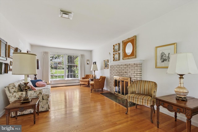 sitting room with visible vents, a baseboard radiator, a brick fireplace, and wood finished floors