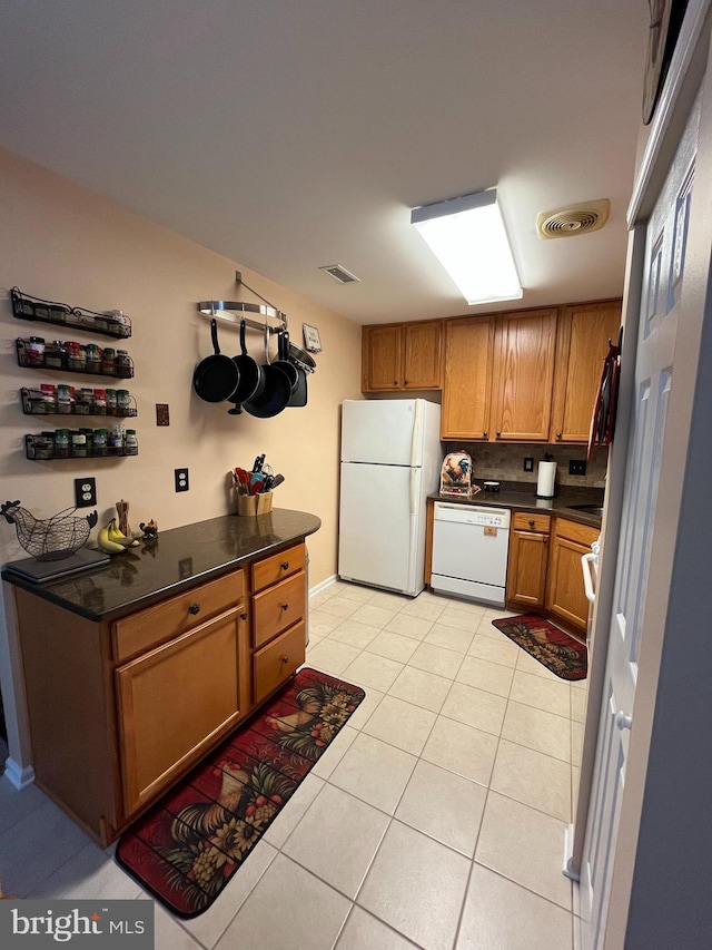kitchen featuring light tile patterned floors, dark countertops, brown cabinets, and white appliances