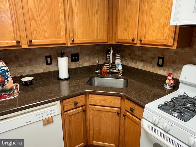 kitchen with brown cabinetry, white appliances, a sink, dark stone countertops, and backsplash