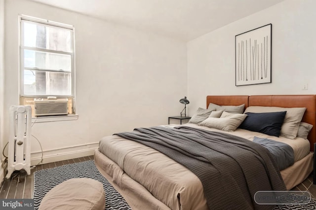 bedroom with baseboards, wood finished floors, radiator heating unit, and cooling unit