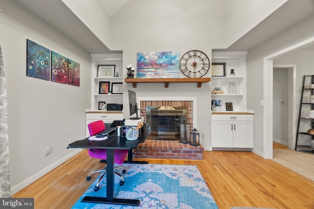 office with a brick fireplace, baseboards, built in shelves, and light wood-type flooring