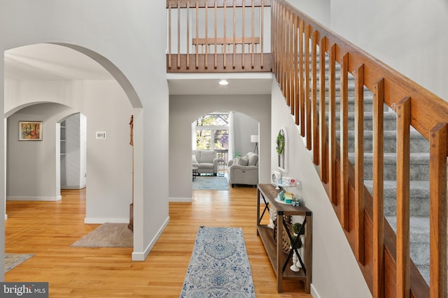 foyer featuring arched walkways, baseboards, wood finished floors, and a high ceiling